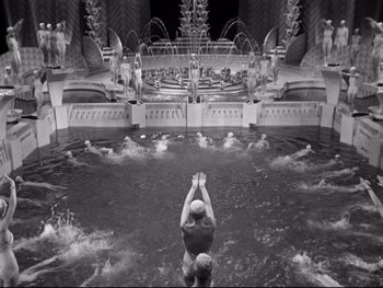 Movie still from “Footlight Parade” (1933), directed by Lloyd Bacon – A man swimming in a pool surrounded by statues; Extreme Wide shot, High angle