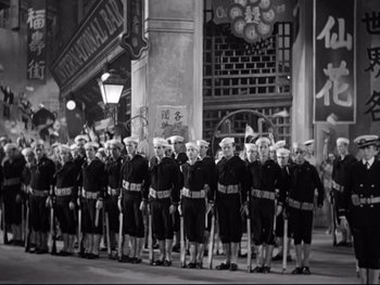 Movie still from “Footlight Parade” (1933), directed by Lloyd Bacon – A group of men in uniform standing next to each other on a street; Wide shot, High angle