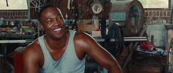 Movie still from “Footloose” (2011), directed by Craig Brewer – A man sitting in a garage smiling for the camera; Close Up shot, Over the shoulder angle