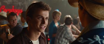 Movie still from “Footloose” (2011), directed by Craig Brewer – A young man smiling at the camera in front of a group of people; Close Up shot, Over the shoulder angle