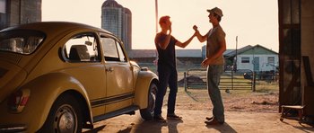 Movie still from “Footloose” (2011), directed by Craig Brewer – Two men shake hands in front of a yellow car; Medium shot, Low angle