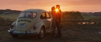 A couple kissing in front of a car at sunset