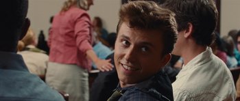 Movie still from “Footloose” (2011), directed by Craig Brewer – A young man smiles for the camera in front of a group of people; Close Up shot, Over the shoulder angle