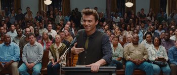 Movie still from “Footloose” (2011), directed by Craig Brewer – A man standing in front of a microphone in front of a group of onlookers; Medium shot, Over the shoulder angle