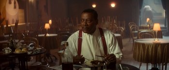 Movie still from “The United States vs. Billie Holiday” (2021), directed by Lee Daniels – A man sitting at a table with a plate in front of him; Medium shot, Over the shoulder angle