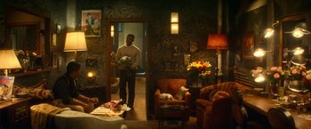 Movie still from “The United States vs. Billie Holiday” (2021), directed by Lee Daniels – A man standing in a living room holding a bouquet of flowers; Wide shot, High angle