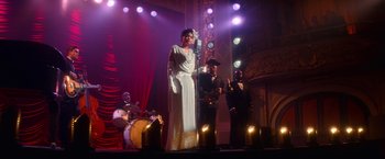 Movie still from “The United States vs. Billie Holiday” (2021), directed by Lee Daniels – A woman in a white dress holding a microphone on a stage; Wide shot, Low angle