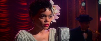 Movie still from “The United States vs. Billie Holiday” (2021), directed by Lee Daniels – A woman with a flower in her hair is singing into a microphone; Close Up shot, Over the shoulder angle