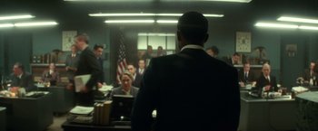 Movie still from “The United States vs. Billie Holiday” (2021), directed by Lee Daniels – A group of people sitting in a room with a flag; Wide shot, Over the shoulder angle