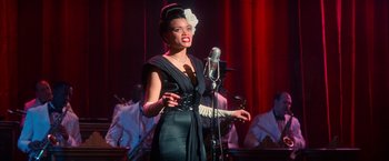 Movie still from “The United States vs. Billie Holiday” (2021), directed by Lee Daniels – A woman in a black dress holding a microphone; Medium shot, Over the shoulder angle