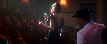 Movie still from “The United States vs. Billie Holiday” (2021), directed by Lee Daniels – A woman in a black dress holding a microphone in front of an audience; Medium shot, Over the shoulder angle