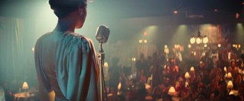 Movie still from “The United States vs. Billie Holiday” (2021), directed by Lee Daniels – A person standing on a stage with a microphone; Medium shot, Over the shoulder angle