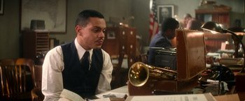 Movie still from “The United States vs. Billie Holiday” (2021), directed by Lee Daniels – A man sitting at a table with a trumpet; Medium shot, Low angle