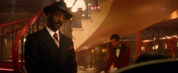 Movie still from “The United States vs. Billie Holiday” (2021), directed by Lee Daniels – A man in a suit and a hat standing next to a man in a red suit; Medium shot, Low angle