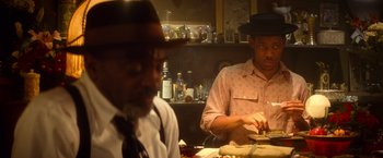 Movie still from “The United States vs. Billie Holiday” (2021), directed by Lee Daniels – Two men sitting at a table in front of a plate of food; Medium shot, Over the shoulder angle