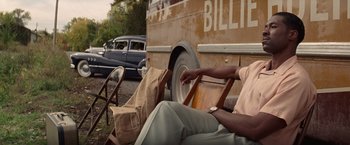 Movie still from “The United States vs. Billie Holiday” (2021), directed by Lee Daniels – A man sitting in front of a bus with a bag on his lap; Medium shot, Over the shoulder angle