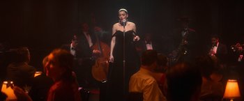 Movie still from “The United States vs. Billie Holiday” (2021), directed by Lee Daniels – A woman in a black dress singing into a microphone; Medium shot, Over the shoulder angle