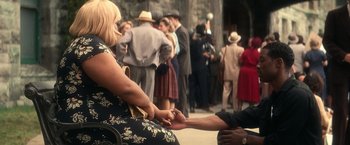 Movie still from “The United States vs. Billie Holiday” (2021), directed by Lee Daniels – A woman sitting on a chair holding a man's hand in front of a crowd of people; Medium shot, High angle