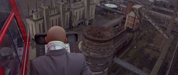 Movie still from “For Your Eyes Only” (1981), directed by John Glen – A man in a suit and tie looking out a window at an abandoned factory; Extreme Wide shot, Overhead angle