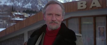 Movie still from “For Your Eyes Only” (1981), directed by John Glen – An older man wearing a red shirt and a fur coat; Close Up shot, Low angle
