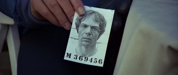 Movie still from “For Your Eyes Only” (1981), directed by John Glen – A person holding a picture of a man with the number m 3 6 9 4 5 6 on it; Extreme Close Up shot, Overhead angle