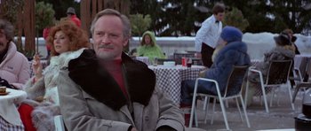 Movie still from “For Your Eyes Only” (1981), directed by John Glen – An older man sitting in front of a group of diners at an outdoor restaurant; Medium shot, Low angle