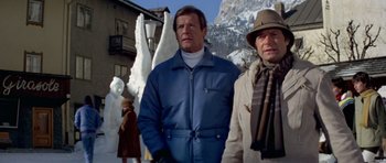 Movie still from “For Your Eyes Only” (1981), directed by John Glen – A man standing next to another man wearing a hat; Medium shot, Low angle