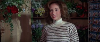 Movie still from “For Your Eyes Only” (1981), directed by John Glen – A woman in a striped sweater standing in front of flowers; Close Up shot, Over the shoulder angle