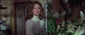 Movie still from “For Your Eyes Only” (1981), directed by John Glen – A woman in a striped sweater standing next to a plant; Medium shot, Over the shoulder angle