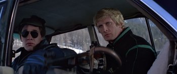 Movie still from “For Your Eyes Only” (1981), directed by John Glen – A man driving a car in the snow with trees in the background; Close Up shot, Low angle