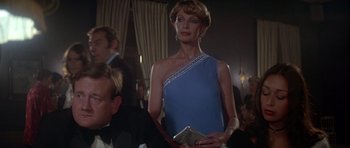 Movie still from “For Your Eyes Only” (1981), directed by John Glen – A woman in a blue dress is holding a silver purse; Medium shot, Low angle