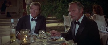 Movie still from “For Your Eyes Only” (1981), directed by John Glen – Two men in tuxedos sitting at a dinner table; Medium shot, High angle