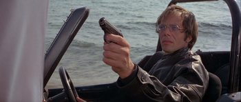 Movie still from “For Your Eyes Only” (1981), directed by John Glen – A man holding a gun while sitting in a car; Close Up shot, Low angle