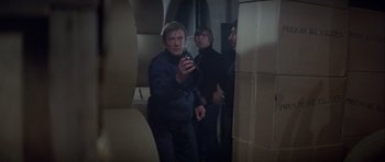 Movie still from “For Your Eyes Only” (1981), directed by John Glen – A group of people standing in a room holding a cell phone; Medium shot, Over the shoulder angle