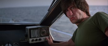 Movie still from “For Your Eyes Only” (1981), directed by John Glen – A man holding a radio in his hand while sitting in a car; Close Up shot, Low angle