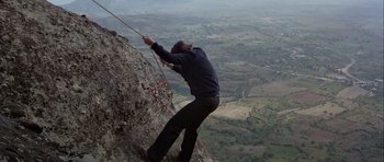 Movie still from “For Your Eyes Only” (1981), directed by John Glen – A man climbing up the side of a rock wall; Extreme Wide shot, Low angle
