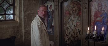 Movie still from “For Your Eyes Only” (1981), directed by John Glen – A man standing in front of a painting of jesus; Medium shot, Low angle
