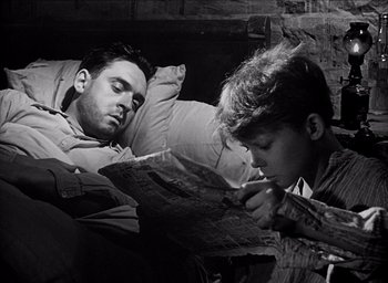 Movie still from “Forbidden Games” (1952), directed by René Clément – A man and a boy are reading a newspaper together; Medium shot, High angle
