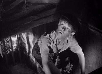 Movie still from “Forbidden Games” (1952), directed by René Clément – A young man in a hat and a shirt looking up; Medium shot, High angle