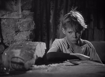 Movie still from “Forbidden Games” (1952), directed by René Clément – A young boy sitting at a table with a knife in his hand; Close Up shot, High angle