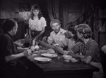Movie still from “Forbidden Games” (1952), directed by René Clément – A group of people sitting around a table eating food; Medium shot, High angle