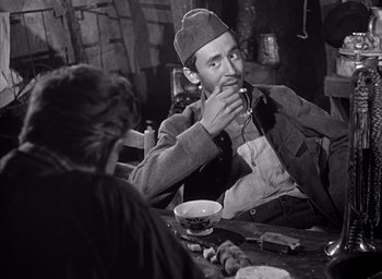 Movie still from “Forbidden Games” (1952), directed by René Clément – A man sitting at a table drinking from a cup; Medium shot, Over the shoulder angle