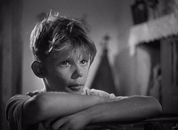 Movie still from “Forbidden Games” (1952), directed by René Clément – Black and white photograph of a young boy leaning on a chair; Close Up shot, Low angle