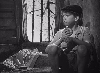 Movie still from “Forbidden Games” (1952), directed by René Clément – A young boy sitting on the ground eating a donut; Medium shot, High angle