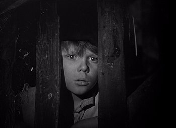 Movie still from “Forbidden Games” (1952), directed by René Clément – A young boy is looking through a wooden fence; Close Up shot, High angle