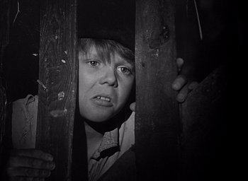 Movie still from “Forbidden Games” (1952), directed by René Clément – A young boy is looking through a wooden fence; Close Up shot, High angle