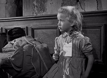 Movie still from “Forbidden Games” (1952), directed by René Clément – A little girl holding a piece of paper in front of a pile of luggage; Medium shot, Over the shoulder angle