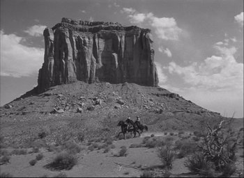 Movie still from “Fort Apache” (1948), directed by John Ford – Two men on horseback in front of a large rock formation; Extreme Wide shot, Low angle