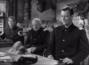 Movie still from “Fort Apache” (1948), directed by John Ford – A group of men sitting at a table in front of a stone wall; Medium shot, Over the shoulder angle