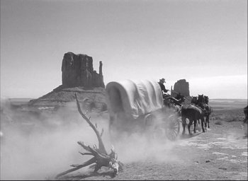Movie still from “Fort Apache” (1948), directed by John Ford – An old photo of a wagon train going down the road; Wide shot, Low angle
